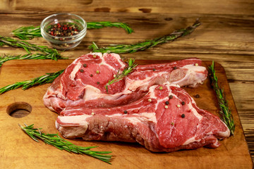 Raw fresh beef rib eye steaks on bone with spices and rosemary on wooden table