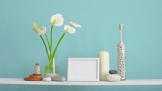 Modern room decoration with crate. Shelf against turquoise wall with decorative cactus, glass and rocks. Hand putting down calla in vase.