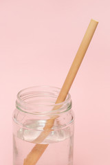 Fototapeta na wymiar Bamboo straw in a glass of water on the pink background, Reusable bamboo straws as an alternative for single-use plastic straws, healthy and sustainable lifestyle concept