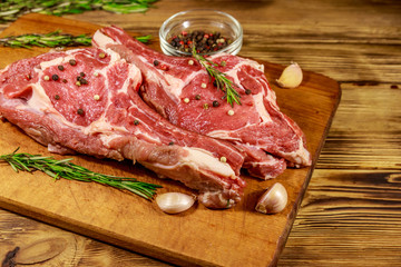 Raw fresh beef rib eye steak on bone with spices, garlic and rosemary on wooden table