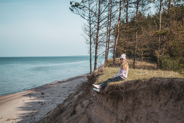 Young adult woman in pink hat sitting alone on the bluffs, looking of sea, freedom concept,...