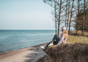 Young adult woman in pink hat sitting alone on the bluffs, looking of sea, freedom concept,...