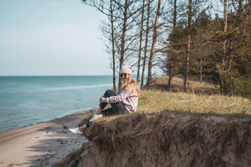 Young adult woman in pink hat sitting alone on the bluffs, looking of sea, freedom concept,...