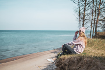 Young adult woman in pink hat sitting alone on the bluffs, looking of sea, freedom concept, peaceful atmosphere, meditation, copy space, Latvia, Jurkalne