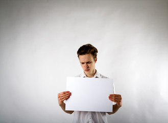 Young man holding white paper in his hands. Unhappy man.