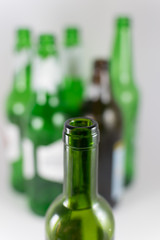 Close-up image of a bottleneck of green wine glass bottle without label with several beer and wine green and brown bottles blurred in the background. Reuse, acoholism, recycle and party concept.