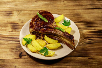 Roasted beef rib eye steak on bone with baked potatoes and herbs on wooden table