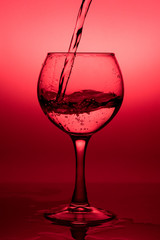 Flowing  liquid (wine) in a glass on a red background