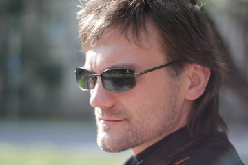 a man in a black jacket and sunglasses in the park