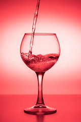 Flowing  liquid (wine) in a glass on a red background