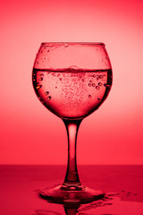Wine glass with liquid (white wine) on a red background