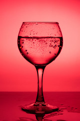 Wine glass with liquid (white wine) on a red background