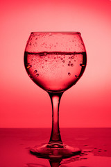 Wine glass with liquid (white wine) on a red background