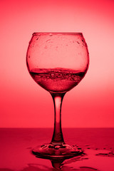 Wine glass with liquid (white wine) on a red background