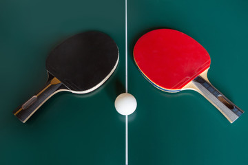 two ping-pong rackets and a ball on a green table.