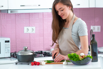 Attractive young cooking woman in apron chopping vegetables for salad for dinner at kitchen at home. Clean healthy food