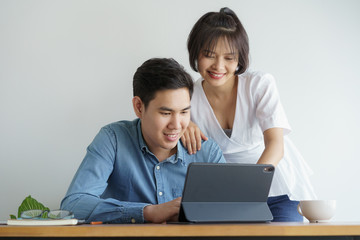 Asian love couple sit  chair in the living room and working on tablet they is smiling happily.