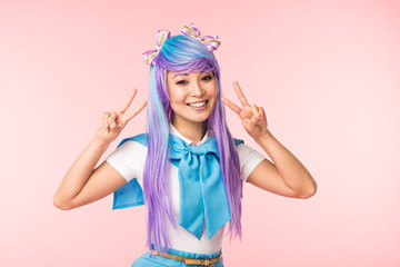 Joyful asian anime girl in purple wig showing peace signs isolated on pink
