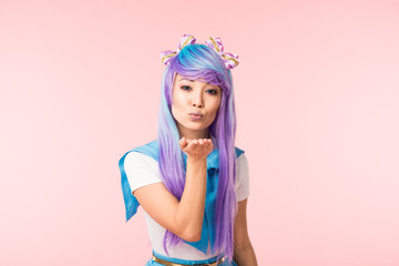 Asian anime girl in purple wig sending air kiss isolated on pink