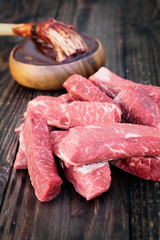 Uncooked raw boneless beef ribs with bowl of barbecue sauce and bbq sauce mop over top a rustic wood table / background. Image shot from overhead view.