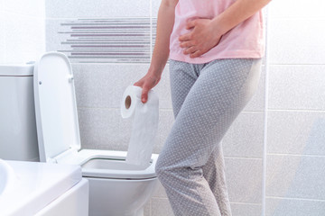 Woman holding a paper roll and suffering from diarrhea, constipation and cystitis at toilet. Stomach and abdominal pain during PMS. Health care