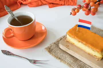 Orange tompouce, traditional Dutch treat with pudding and frosting on national holiday Kings Day (April 27th), in The Netherlands. With cup of tea and Dutch flag