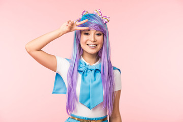 Blissful asian anime girl in purple wig showing peace sign isolated on pink