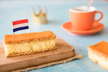 Orange tompouce, traditional Dutch treat with pudding and frosting on national holiday Kings Day (April 27th), in The Netherlands. With cup of coffee, crown and Dutch flag