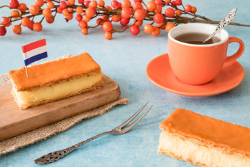 Orange tompouce, traditional Dutch treat with pudding and frosting on national holiday Kings Day (April 27th), in The Netherlands. With cup of tea, fork and Dutch flag