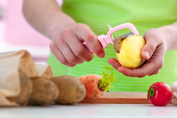 Housewife in apron peeling ripe potato with a peeler for cooking fresh vegetable dishes at home. Proper healthy eating and clean food