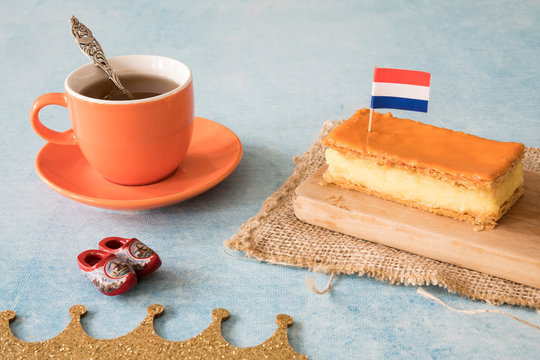 Orange tompouce, traditional Dutch treat with pudding and frosting on national holiday Kings Day (April 27th), in The Netherlands. With cup of coffee, wooden shoes and Dutch flag