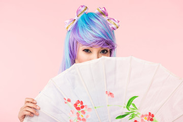 Asian anime girl in wig holding paper umbrella isolated on pink