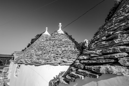 Cityscape with typical amazing architecture of truli with beautiful roofs lighted by the Sun in Puglia region, near the town of Alberobello, Southern Italy. Warm summer morning, black and white