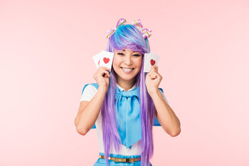 Happy asian anime girl in purple wig holding cards with hearts isolated on pink