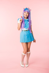 Full length view of smiling asian otaku girl holding lollipop on pink