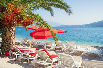 Summer beach vacation.  Sunny Mediterranean landscape with red beach umbrellas. Montenegro, Adriatic Sea,  Bay of Kotor, Herceg Novi