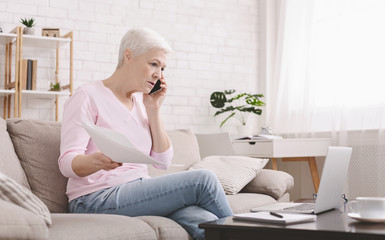 Upset senior woman talking on phone and working at home