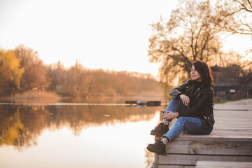 young pretty fashion woman sitting on pier on sunset with beautiful view of river