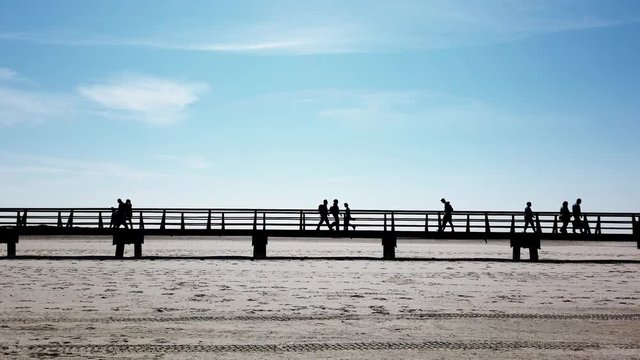 unrecognizable group of people in silhouette walking on walkway or bridge across beach at German seaside resort St. Peter-Ording