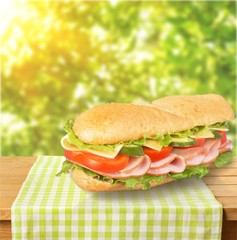 Long baguette sandwich with lettuce, vegetables, ham, and cheese on white background