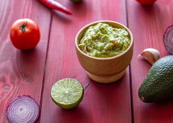 Guacamole and ingredients. Red background. Mexican cuisine.