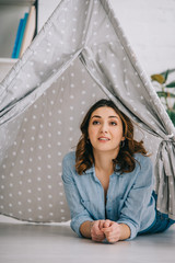 Inspired young woman lying in grey wigwam at home © LIGHTFIELD STUDIOS