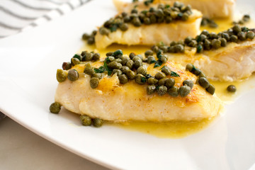 Seared Grouper Fillets with Lemon-Caper Butter: Four whitefish fillets drizzled with lemon-butter sauce and topped with capers and chopped parsley