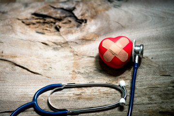 Cushioned Plaster Strip Medical Patch First Aid Band Glued on a red heart on a wooden floor.
