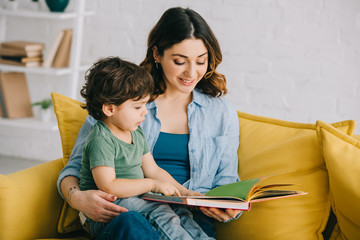 Mom and son sitting on yellow sofa and reading book