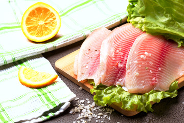 Tilapia fillet with lemon, rosemary and lettuce on a cutting board.