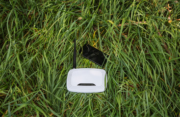 Wi-Fi router and smartphone standing in the green grass. Internet connection in the nature. Forest...