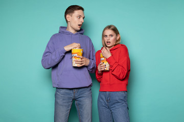 Scared young couple in casual clothes eating popcorn