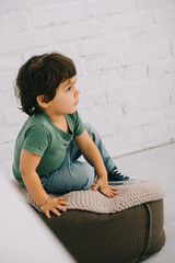 Obraz premium Child in green t-shirt sitting on pouf on floor