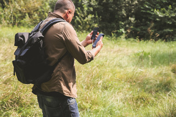 Tourist with smartphone and battery charger is looking for the way in summer forest. Guy with powerbank is lost in the nature. Modern technologies concept to stay always online and in touch.